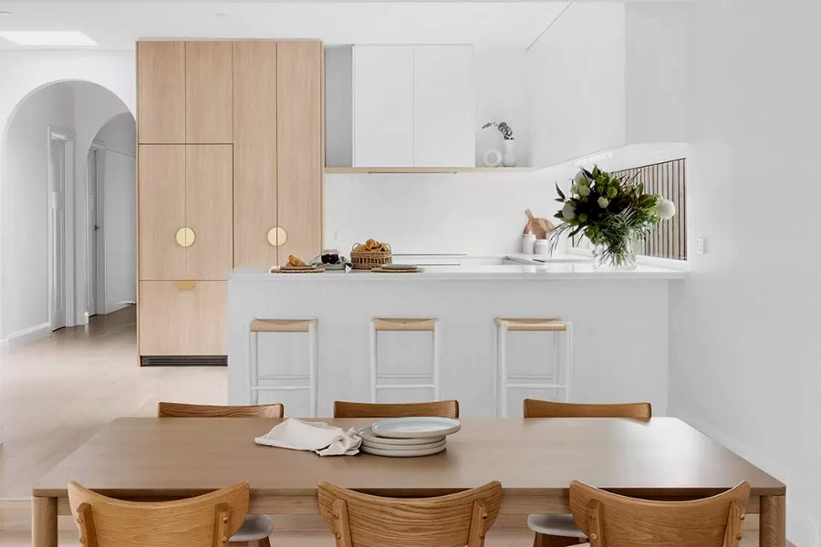 A custom made bespoke white modern kitchen with white oak details and an integrated fridge.