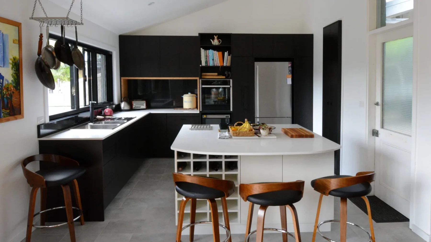 Sleek black custom-made kitchen with slab bench tops and dark veneer cabinets with white poly island unit with wine rack. A combination of top-quality joinery and marble surfaces delivers a space that is gorgeous. Custom-made joinery and cabinet making.